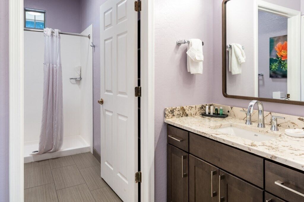 Une salle de bain avec une douche, un lavabo doté d’un plan de toilette en marbre et un miroir orné d’une peinture de fleurs.