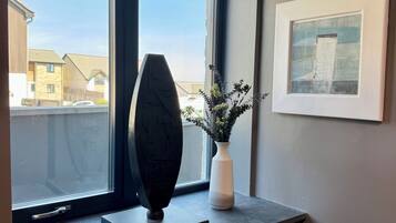 Una habitación con ventana, un jarrón con flores y un cuadro en la pared.