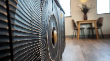 A close-up of a textured, metallic surface with a circular design element, likely part of a piece of furniture or decor. In the background, there is a dining area with a table and chairs, and a window allowing natural light to enter.