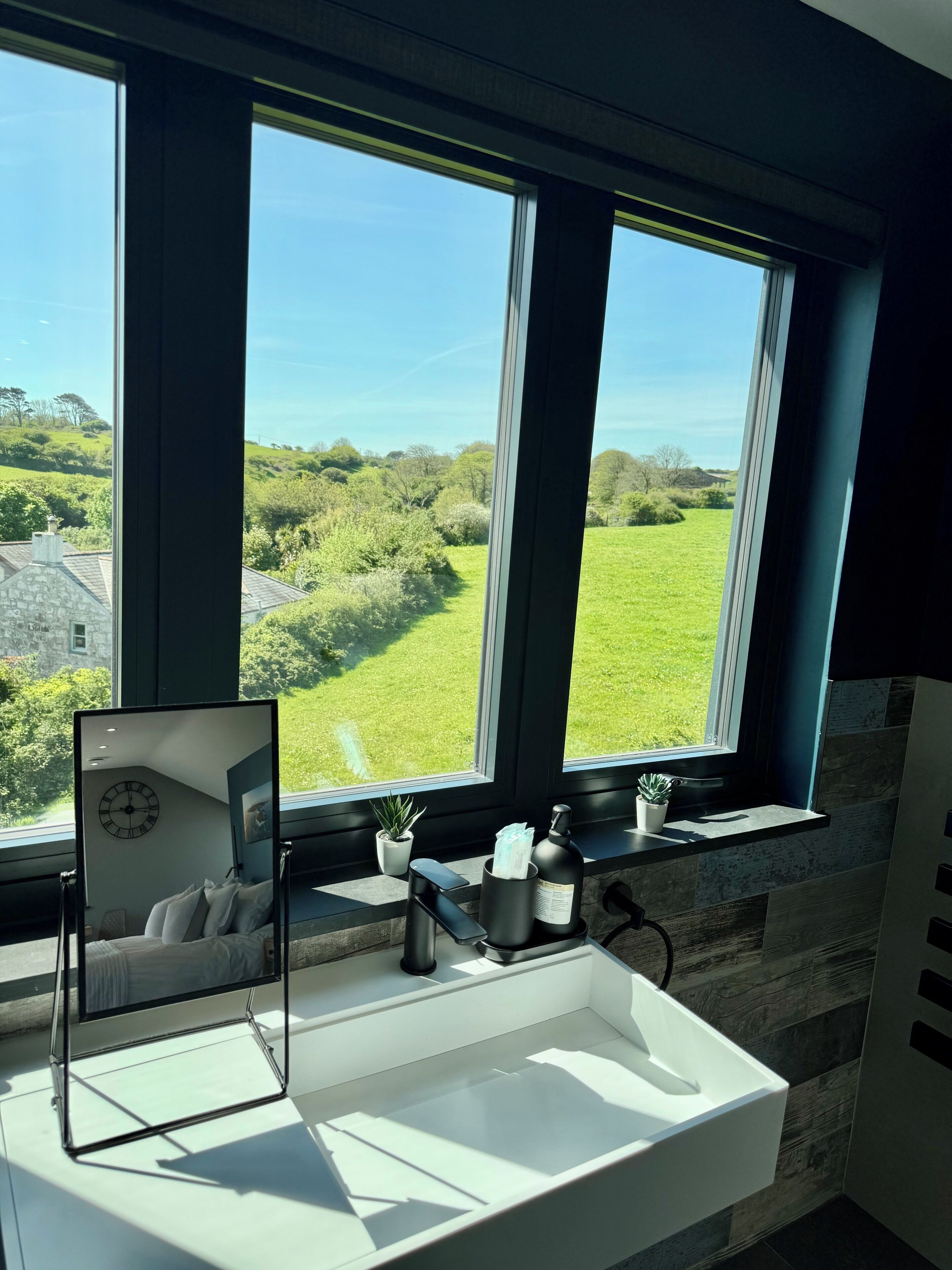 A modern bathroom with a large window, a sink, and a mirror.