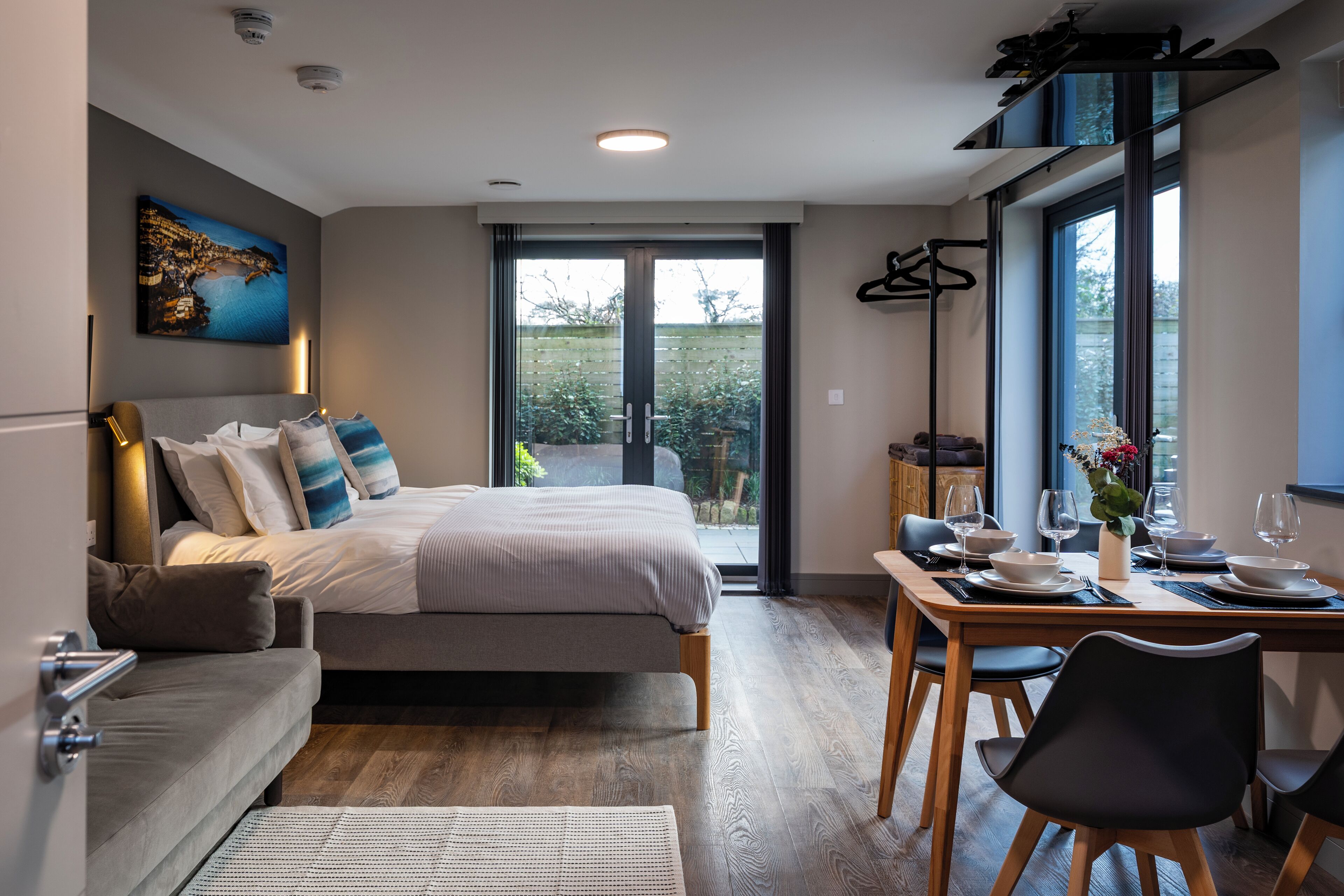 A modern bedroom with a bed, bedside table, and a view of the outdoors through a glass door.