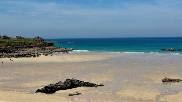 A beach with clear skies, rocky outcrops, and calm sea. - Uno Carbis Bay (St Ives)