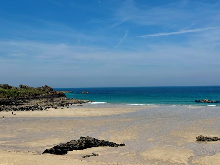 A beach with clear skies, rocky outcrops, and calm sea.