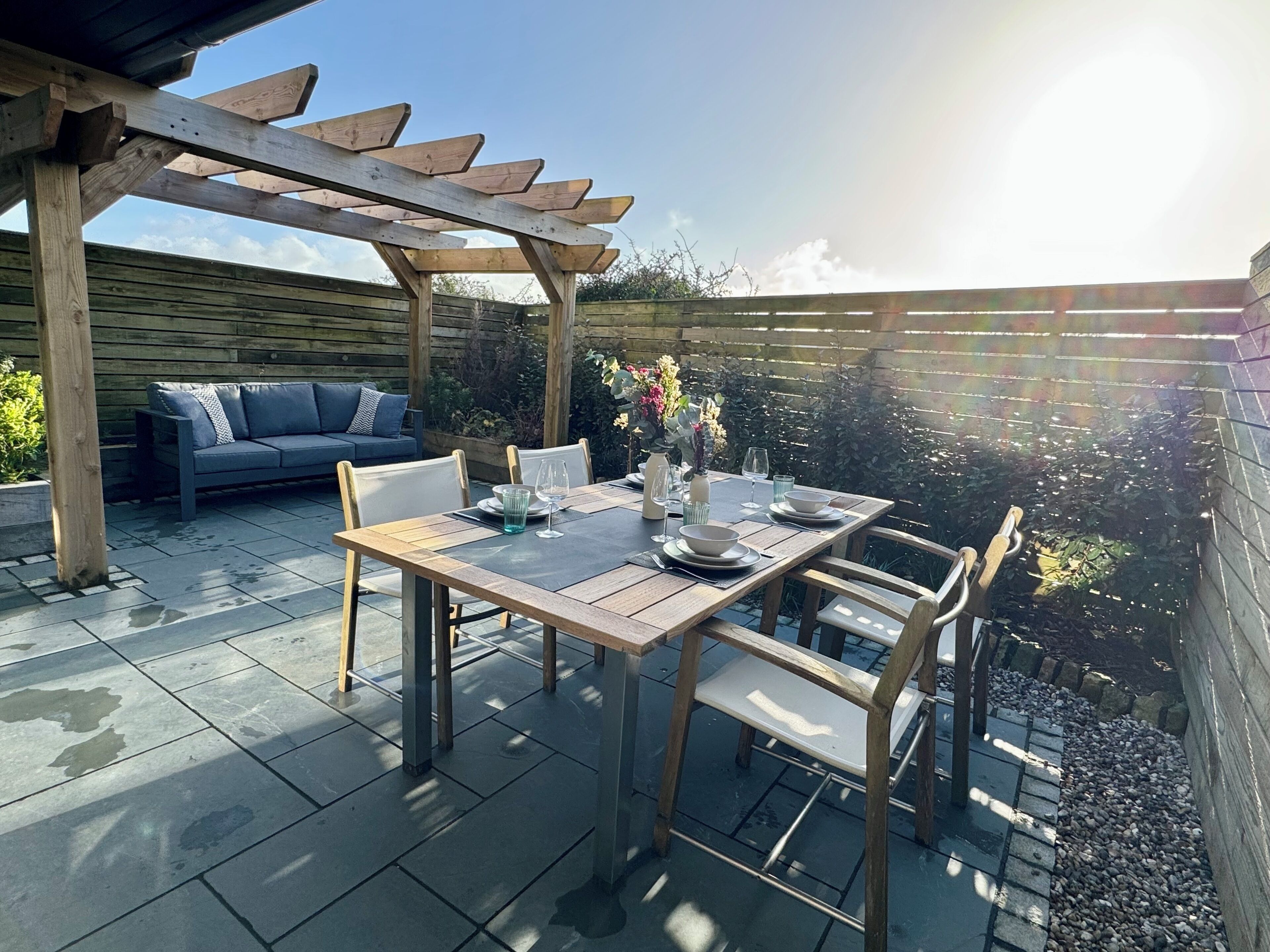 Eine Terrasse mit Holztisch und -stühlen, einer Sitzecke und einer Pergola.