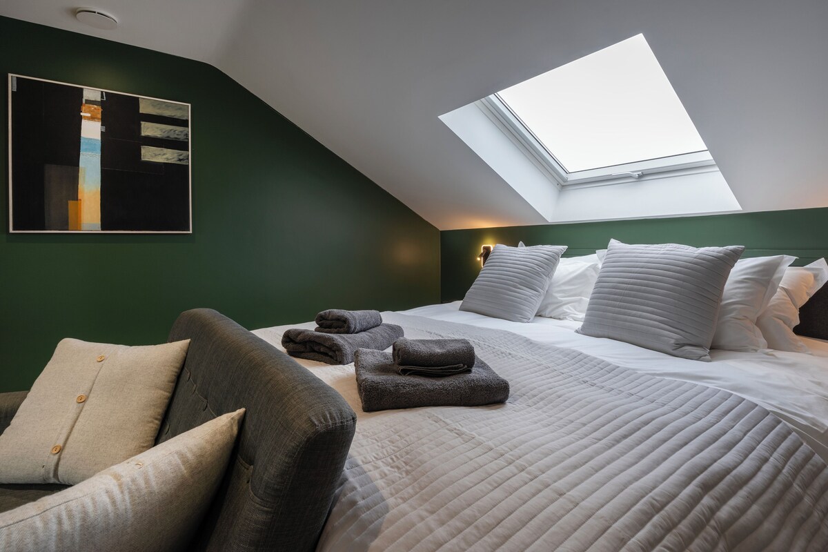 A bedroom with a skylight, a bed with white linens, and a grey sofa.