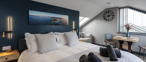 A modern hotel room with a large bed, a desk, a chair, and a view of the sea through a skylight.