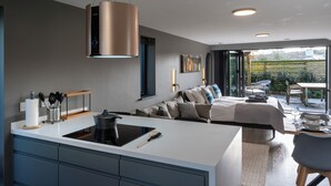 A modern kitchen with a central island, a dining area with a table and chairs, a large bed with a view, and a balcony with outdoor seating. - Uno Carbis Bay (St Ives)