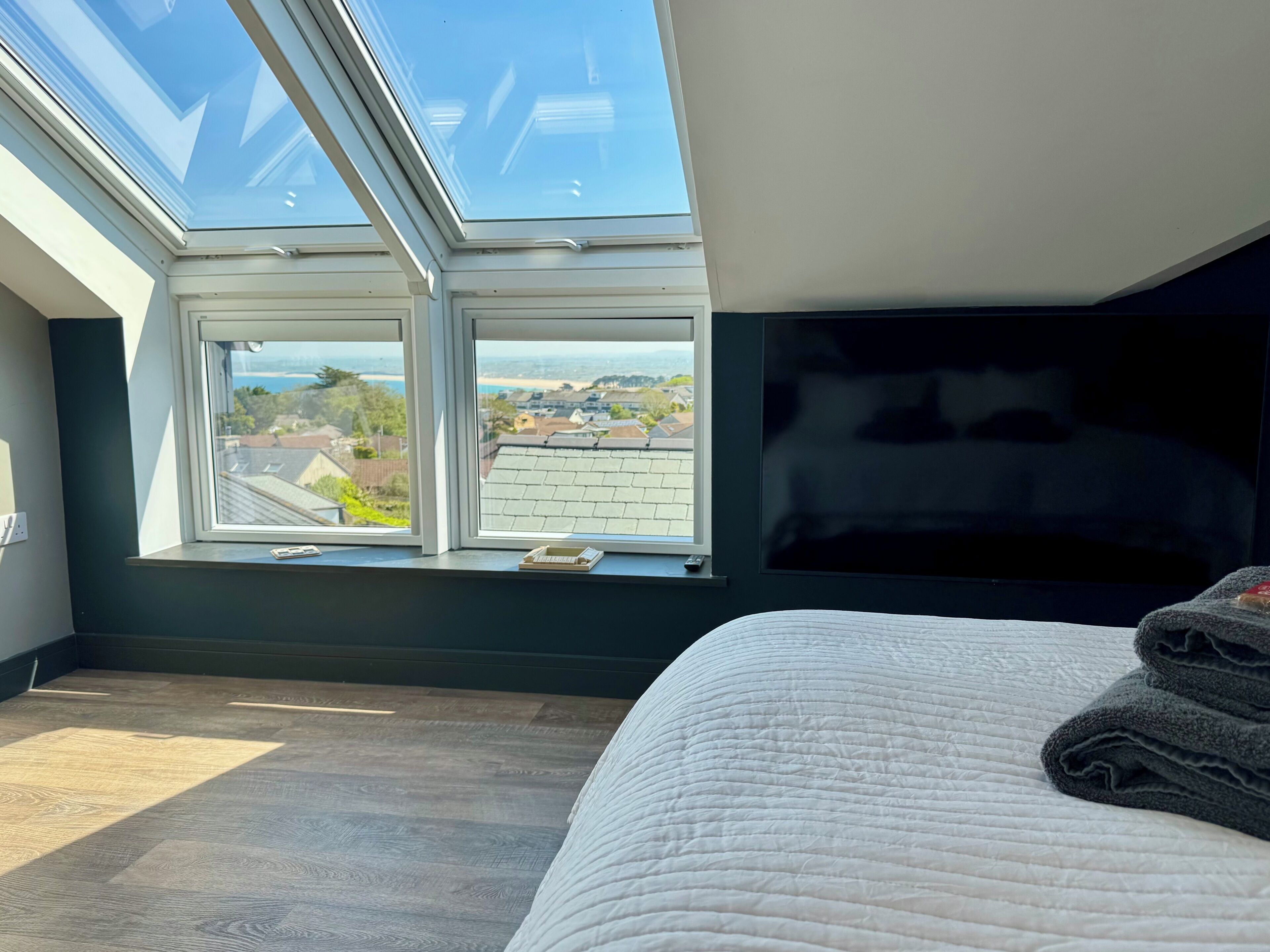 A bedroom with a skylight, a bed, and a view of a residential area.