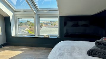 Quarto com claraboia, cama e vista para uma área residencial.