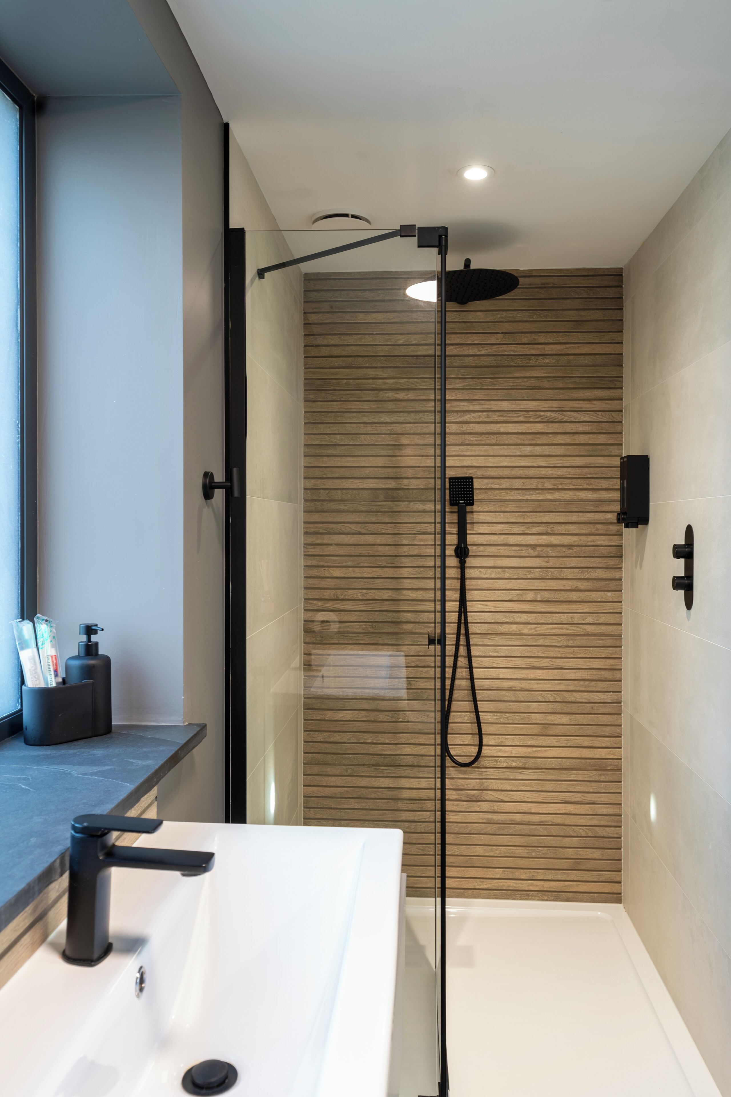 Un bagno moderno con un lavandino bianco, un soffione a mano e una parete in legno.
