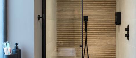 Un bagno moderno con un lavandino bianco, un soffione a mano e una parete in legno.