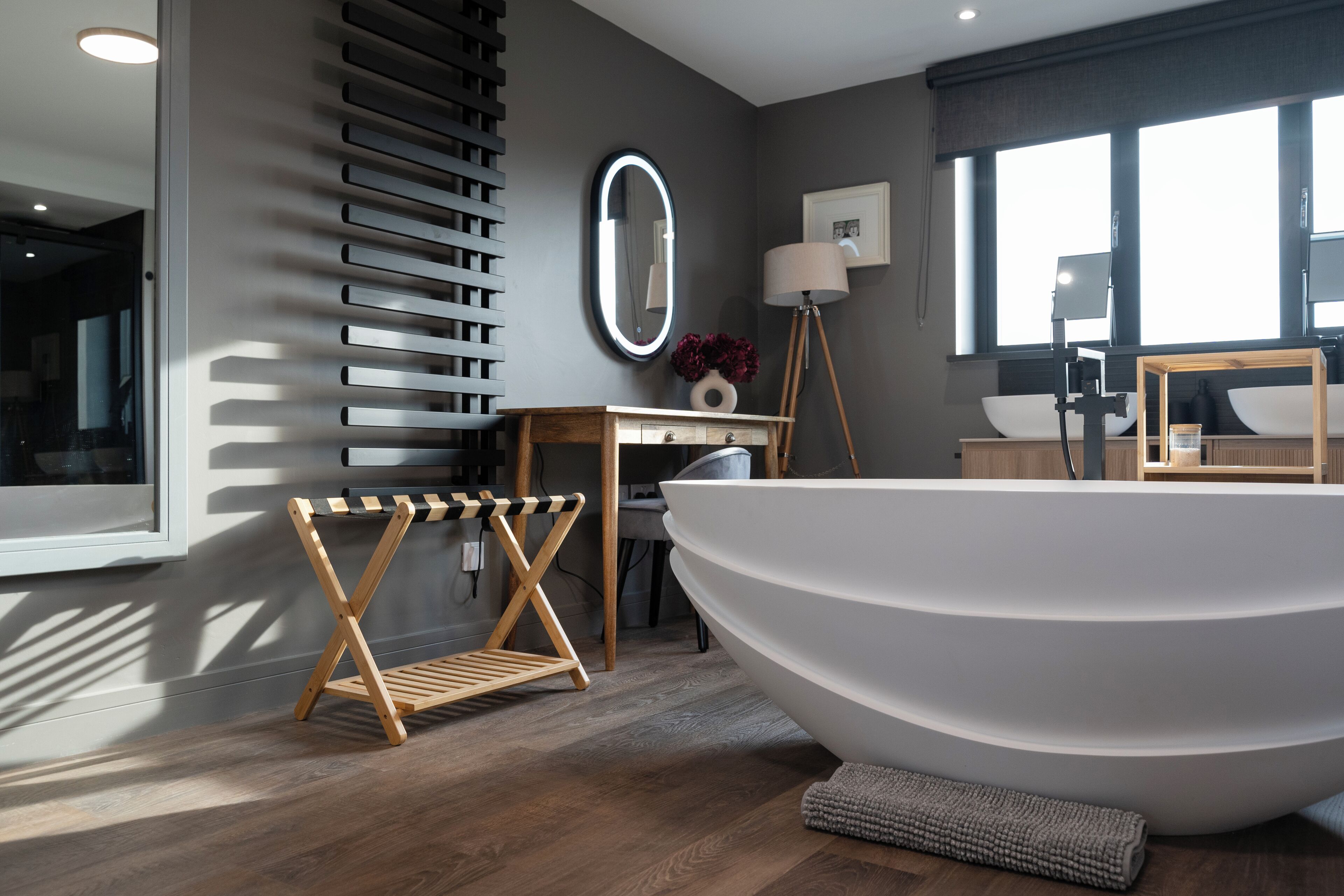 A modern bathroom with a large freestanding bathtub, a vanity with a mirror, and a floor lamp.