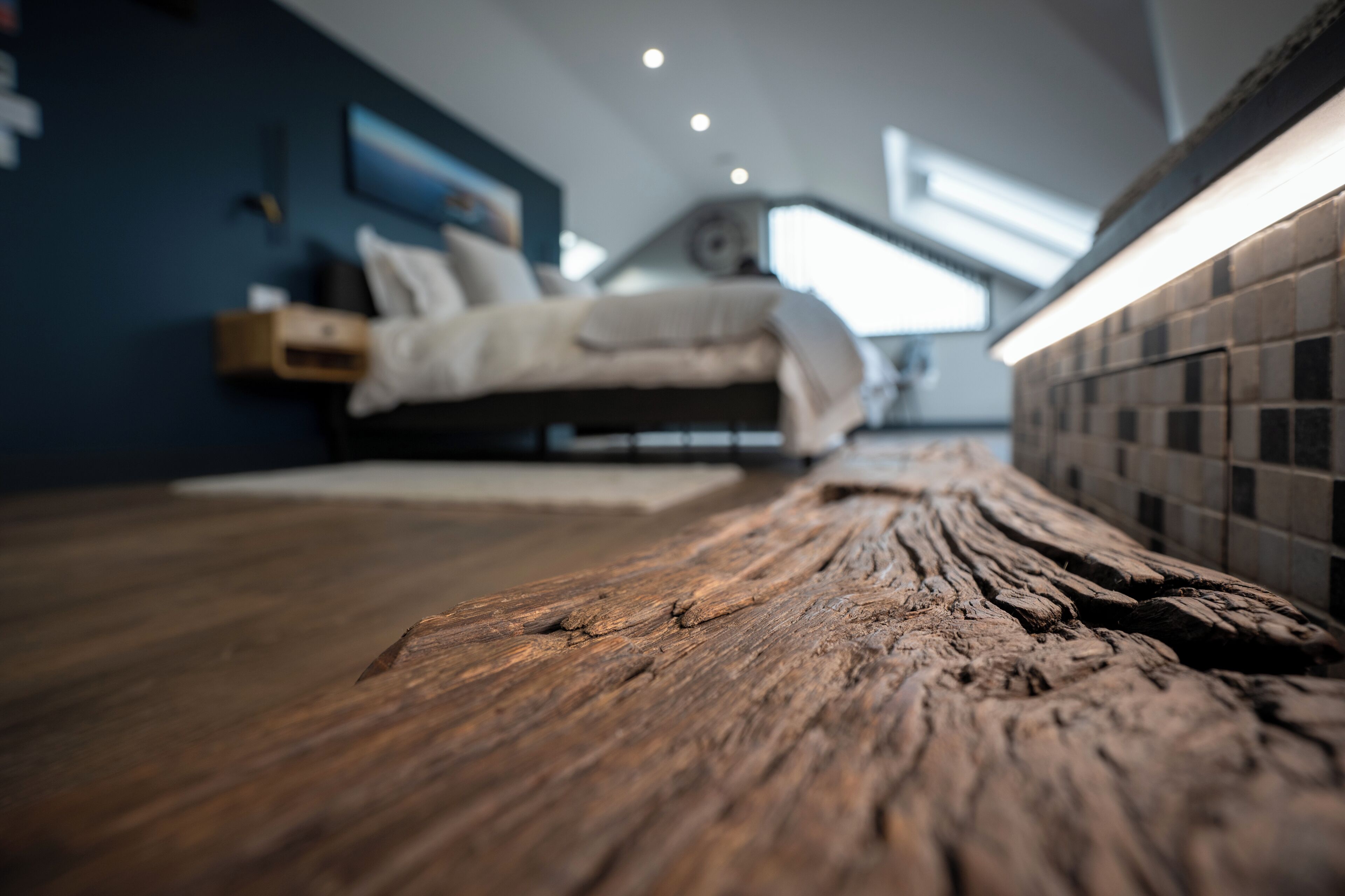 Un plancher en bois mène à un lit doté d’une tête de lit, d’une table de chevet et d’une horloge fixée au mur.