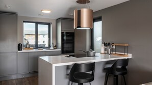 A modern kitchen with a central island, bar stools, and a pendant light. - Uno Carbis Bay (St Ives)