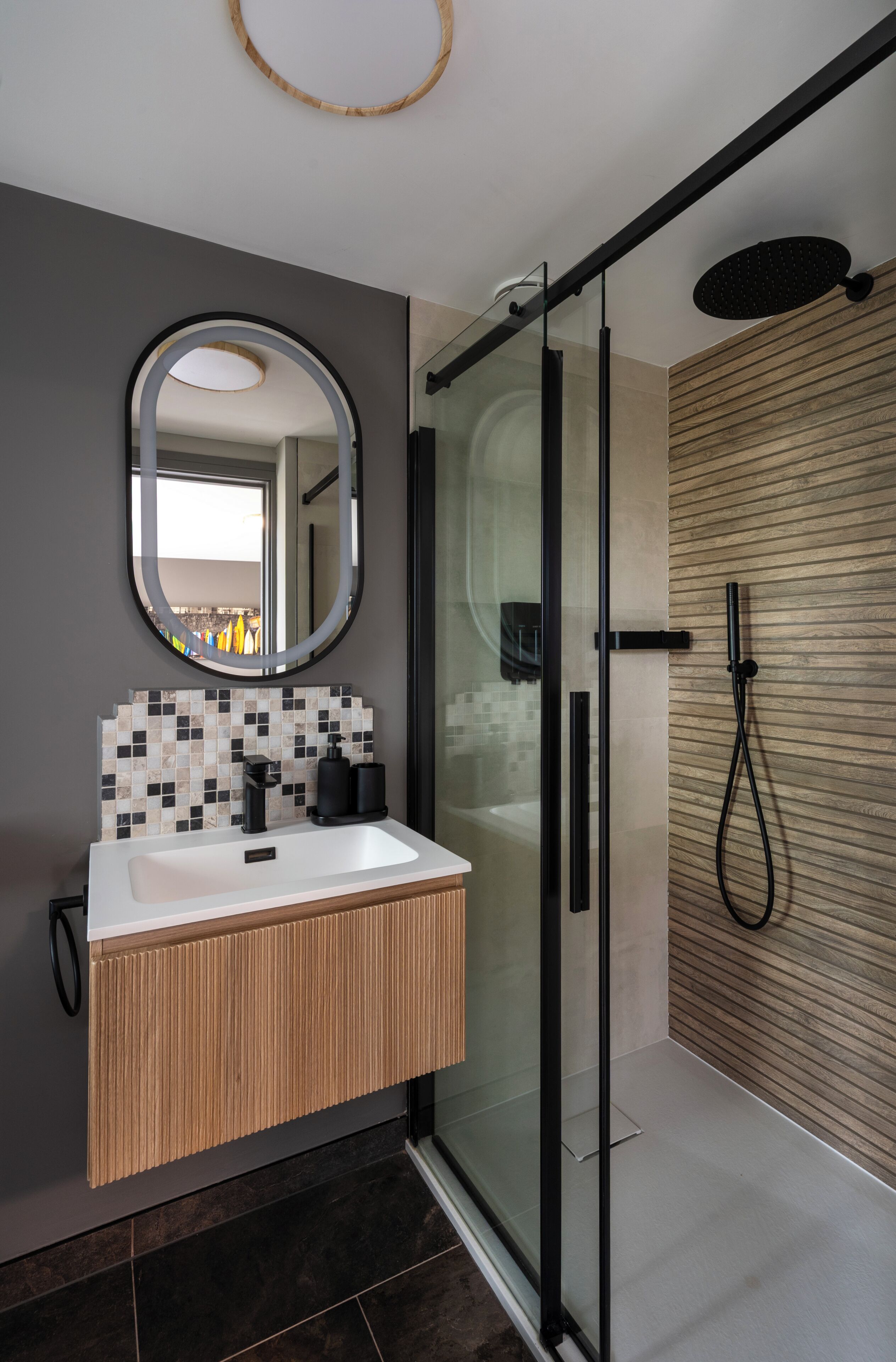 A modern bathroom with a glass shower enclosure, a white sink with a wooden vanity, and a mirror with a circular frame.