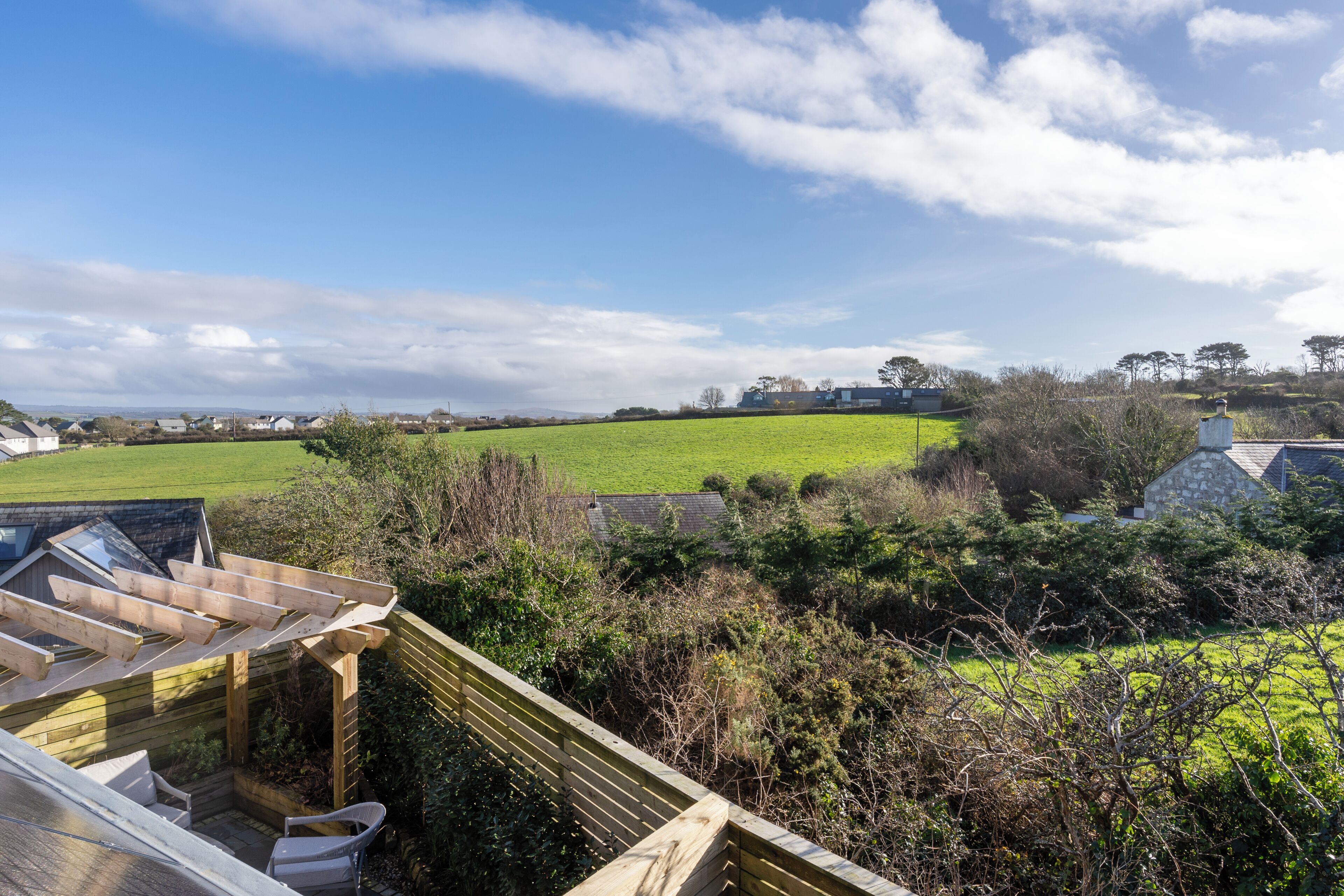 Vista de una propiedad en el campo con un pérgola de madera, un edificio de piedra y un campo verde.