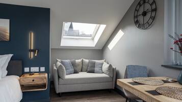 A modern room with a loft bed, a sofa, a dining table, and a skylight.