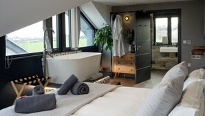 A modern bedroom with a large bed, a bathtub, and a view of the outdoors. - Uno Carbis Bay (St Ives)