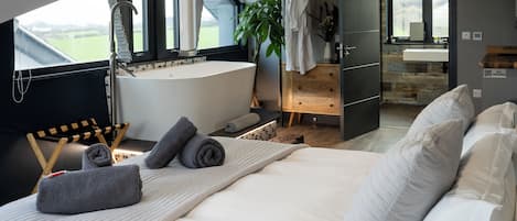 A modern bedroom with a large bed, a bathtub, and a view of the outdoors.