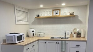 A modern kitchen with white cabinets, a microwave, a toaster, and a sink. There is a wooden countertop and a woven placemat on the table. -  Gertie's Nook: Charming Private Studio Space close to everything! (Dartmouth)