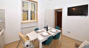 Ein Essbereich mit einem für zwei Personen gedeckten Tisch, einem Stuhl, einem Heizkörper und einem an der Wand befestigten Fernseher.