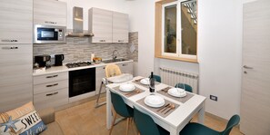 Una cocina moderna con microondas, estufa y lavaplatos. Hay una mesa de comedor lista con platos, cubiertos y una copa de vino.