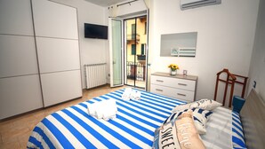 Ein Schlafzimmer mit Bett, Kommode, Fernseher und Balkonblick.
