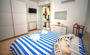 A bedroom with a bed, a dresser, a TV, and a balcony view.