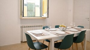 Ein Essbereich mit einem weißen Tisch, gedeckt für vier Personen, grünen Stühlen und einem Fenster mit Blick auf Gebäude.
