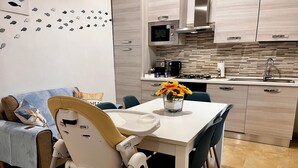 Eine moderne Küche mit Mikrowelle, Herd und Spüle. Ein Esstisch mit Stühlen und einem Hochstuhl für Babys steht bereit.