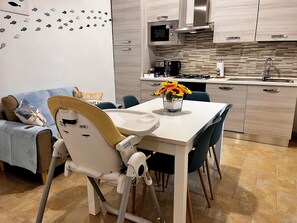 Eine moderne Küche mit Mikrowelle, Herd und Spüle. Ein Esstisch mit Stühlen und einem Hochstuhl für Babys steht bereit.
