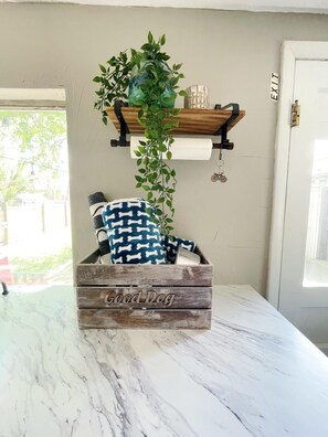 A rustic wooden crate with a 'Good Dog' inscription on a marble countertop, a hanging plant, and a patterned pillow. - Peach Tree: Sunshine & Game Room Fun (Fruita)