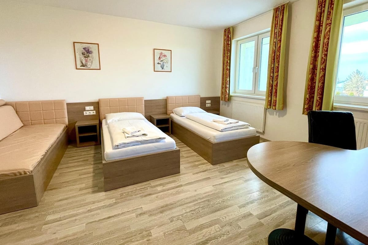Hotellihuone, jossa on kaksi erillistä sänkyä, sohva, ruokapöytä ja kaksi kehystettyä kuvaa seinällä.
