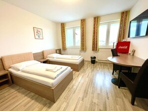 Habitación de hotel con dos camas, una mesita, una silla, un televisor y un refrigerador Coca-Cola.