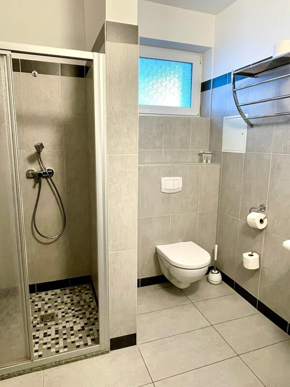 Een badkamer met een douche, toilet en een raam.