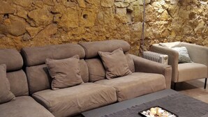A living room with a stone wall, a sectional sofa, a smaller armchair, and a coffee table with decorative items. - MONUMENT, large, cosy apartment (Barcelona)