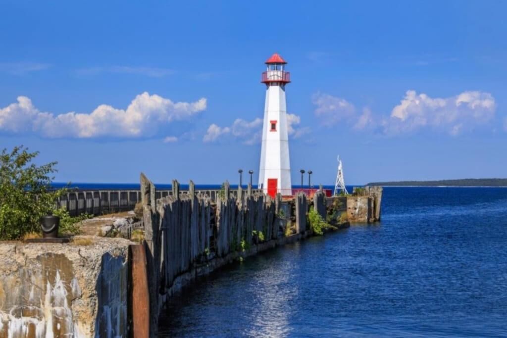 Un phare au bord de la mer, avec une jetée en bois qui s’avance dans l’eau.