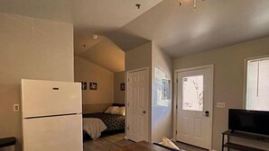 Un espacio habitable compacto con kitchenette, una cama, ventilador de techo y televisor.