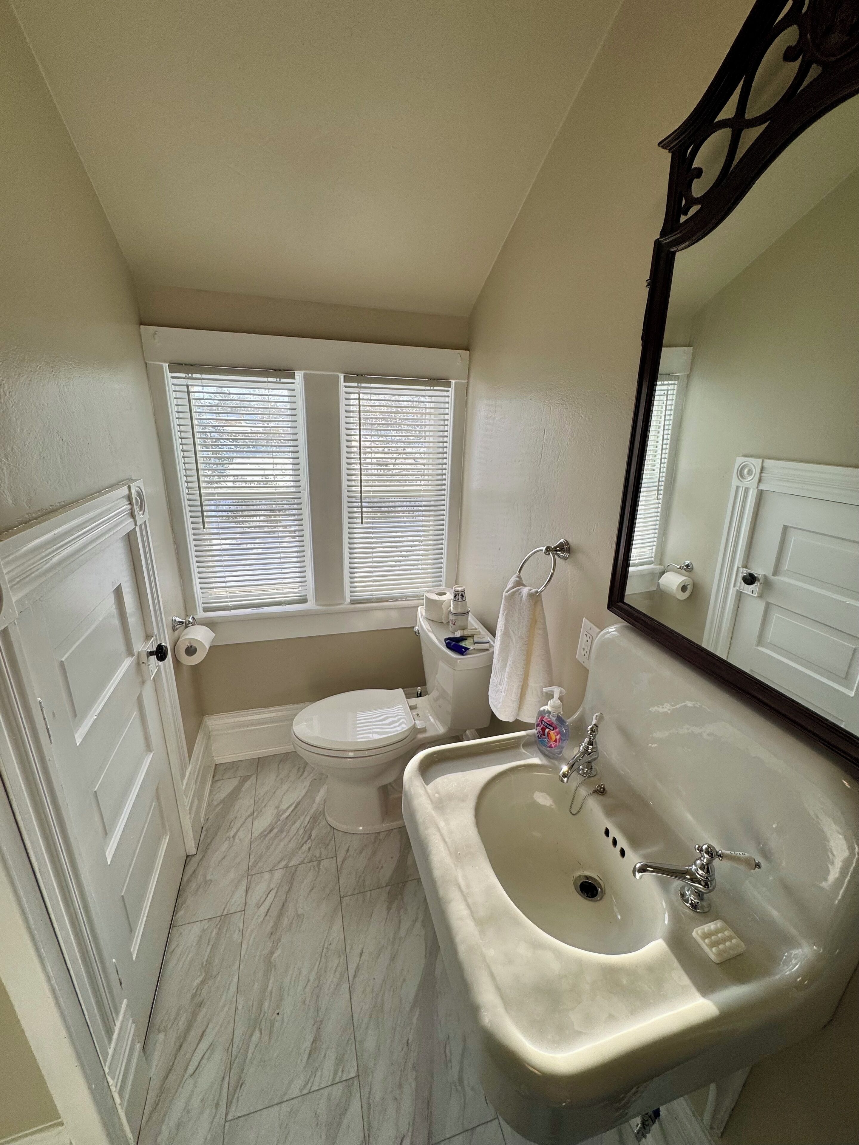 A bathroom with a toilet, sink, and window with blinds.