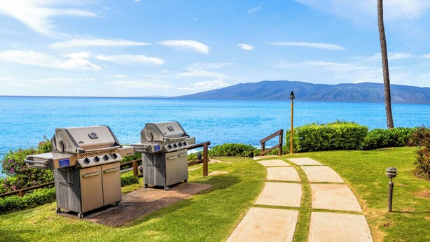 A patio with two barbecue grills, a pathway, and a view of the sea and mountains. - Kuleana Club - 210 (Lahaina)