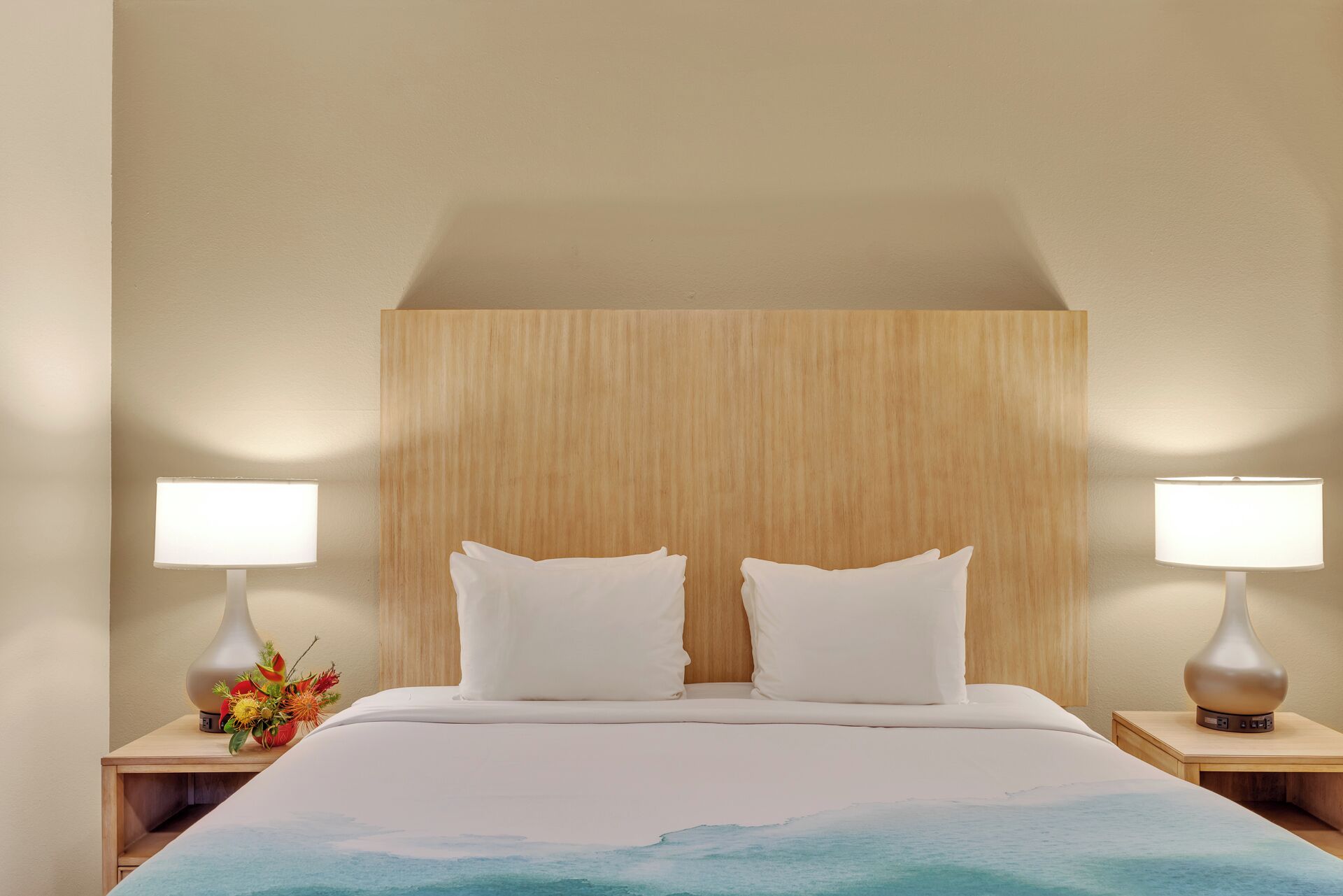A hotel room with a large bed, two bedside lamps, and a wooden headboard.