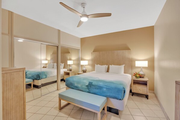 A hotel room with a large bed, a bench, a nightstand, a mirror, and a ceiling fan. - Kuleana Club - 210 (Lahaina)