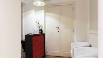 A hotel room with a red and black desk, a white sofa, a white wardrobe, and a hanging lamp.