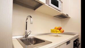 A kitchen with a stainless steel sink, a microwave above it, and a fruit bowl on the counter. - History Suite Essence (Rome)