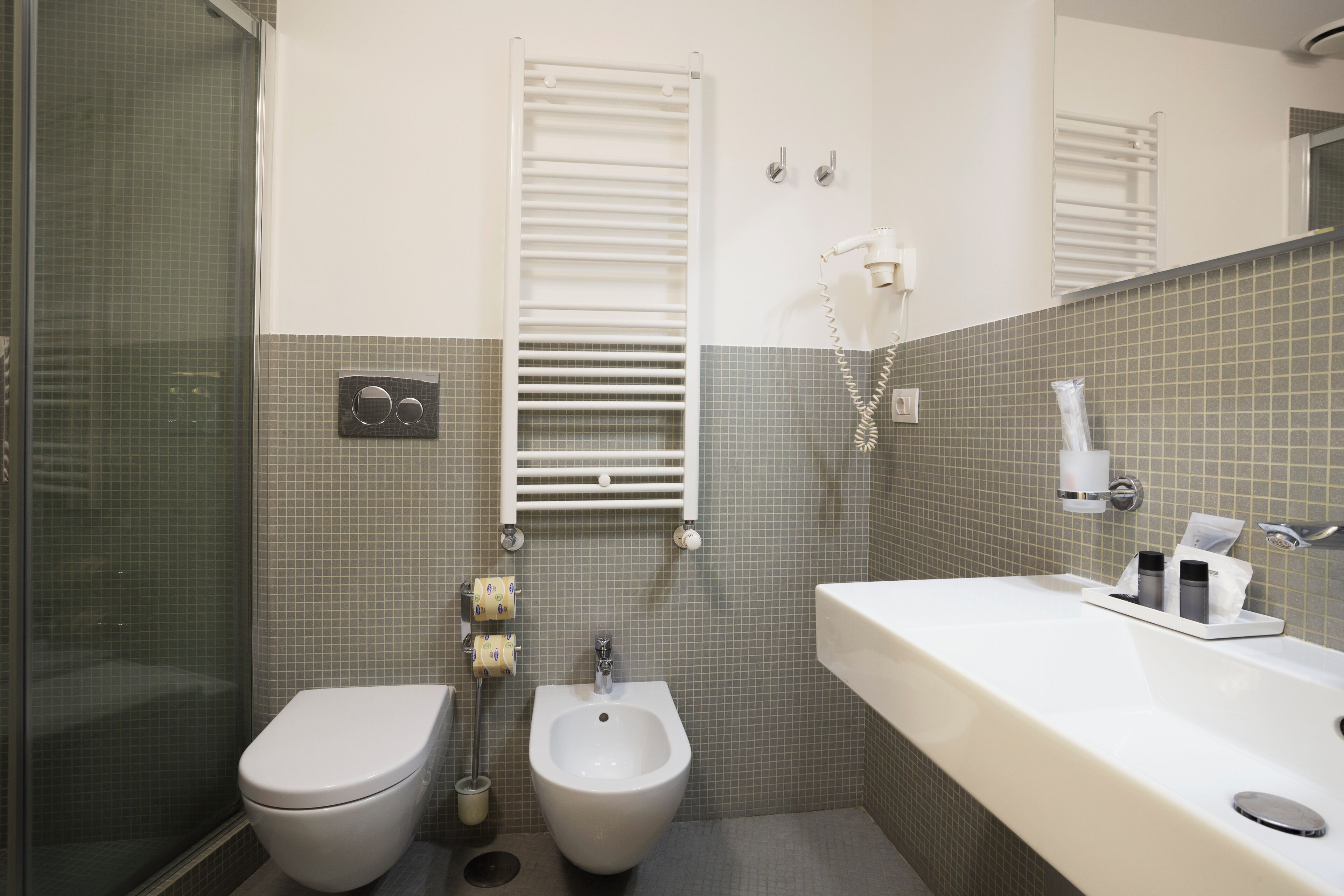 Un baño con inodoro, bidé, lavamanos y un perchero para toallas.