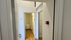 A hallway with wooden flooring, white walls, and a door leading to a room with a toilet. - History Suite Essence (Rome)