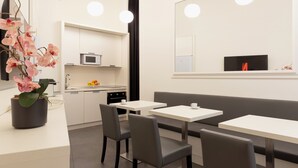 A modern hotel room with a kitchenette, a dining area with a bench and tables, and a large mirror on the wall. - History Suite Essence (Rome)