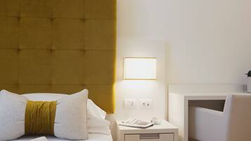 A hotel room with a tufted headboard, a bedside table with a lamp, a chair, and a nightstand with a phone and a cup.