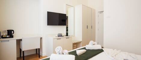 A hotel room with a bed, a desk with a computer, a TV, and a wardrobe.