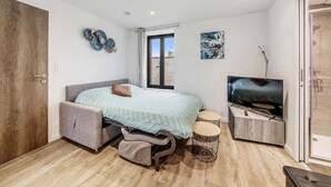Un dormitorio con cama, televisión, una mesita pequeña y un banco.